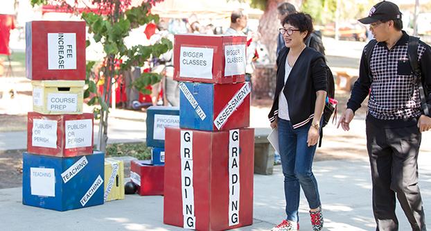 Students walk passed boxes that the Fresno State CFA chapter used in a skit called “Race to the Bottom” to illustrate the plight of CSU faculty and students on Thursday in front of the Kennel Bookstore. Paul Schlesinger / The Collegian