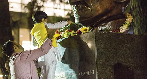 A child places a flower on the Mahatma Gandhi’s statue at the Peace Garden area to celebrate his 147th birthday on Oct. 5, 2016. (Khone Saysamongdy/The Collegian)