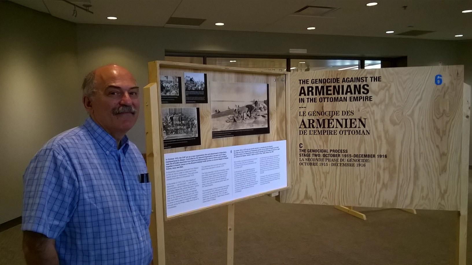 Barlow Barlow DerMugrdechian stands next to an exhibit for an upcoming genocide presentation in the Henry Madden Library. (Sabrina Stevenson)