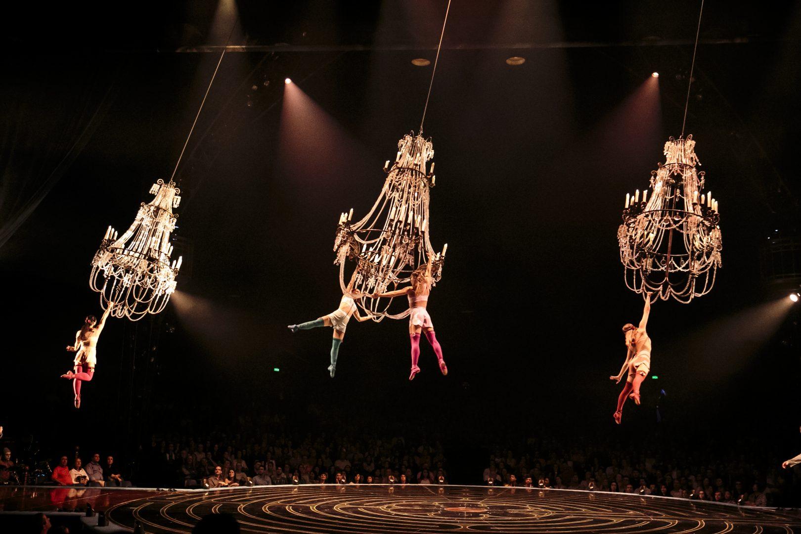 Aerialists perform on swinging chandeliers.