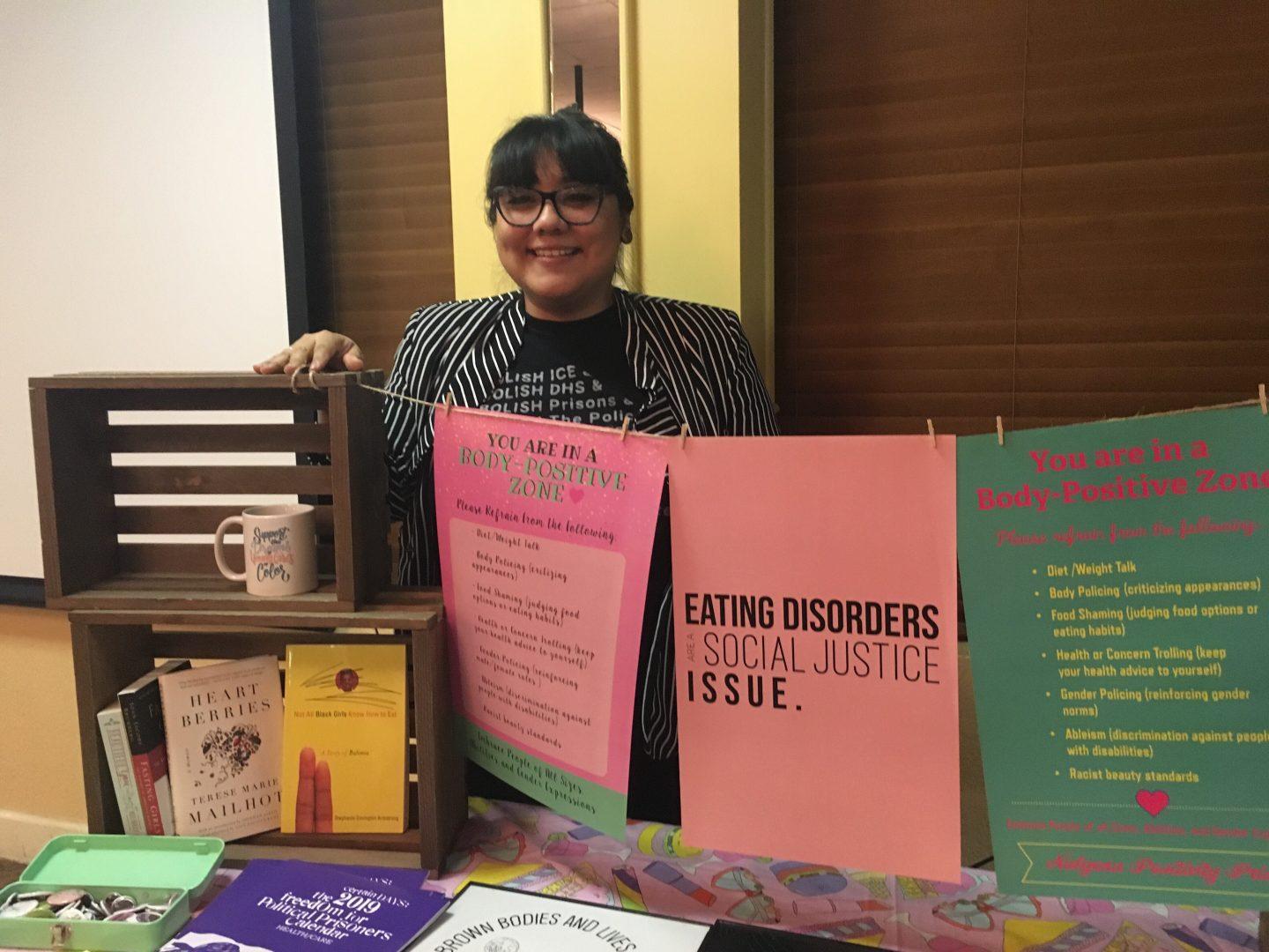 Gloria Lucas stands with literature and signs promoting body pride and positive self-image. (Melina Ortiz/The Collegian)