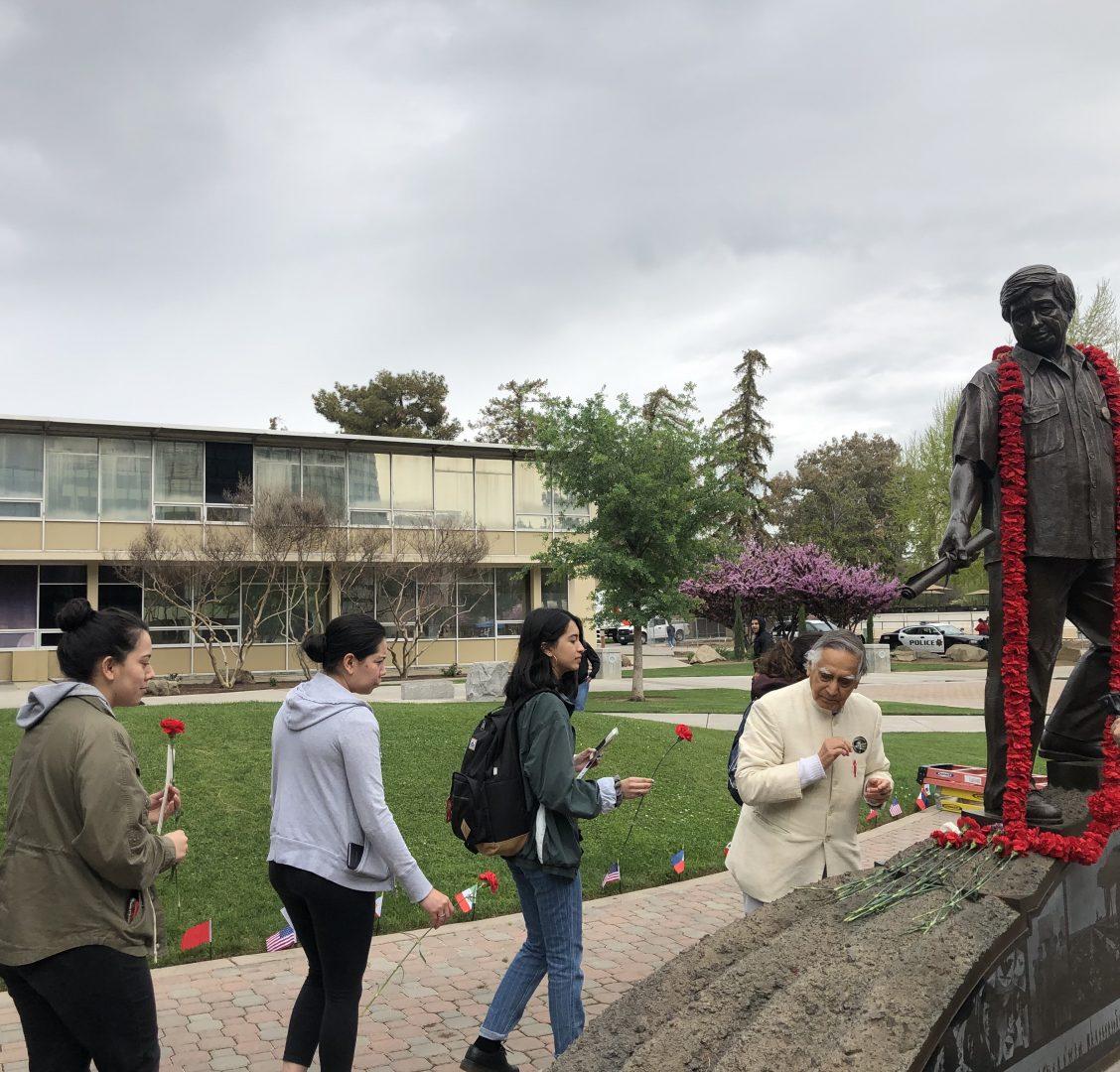Dr. Sudarshan Kapoor (right) helps Fresno State students arrange red carnations on the Cesar Chavez statue in the Peace Garden after the celebration on March 27. (Andrea Marin Contreras/The Collegian)