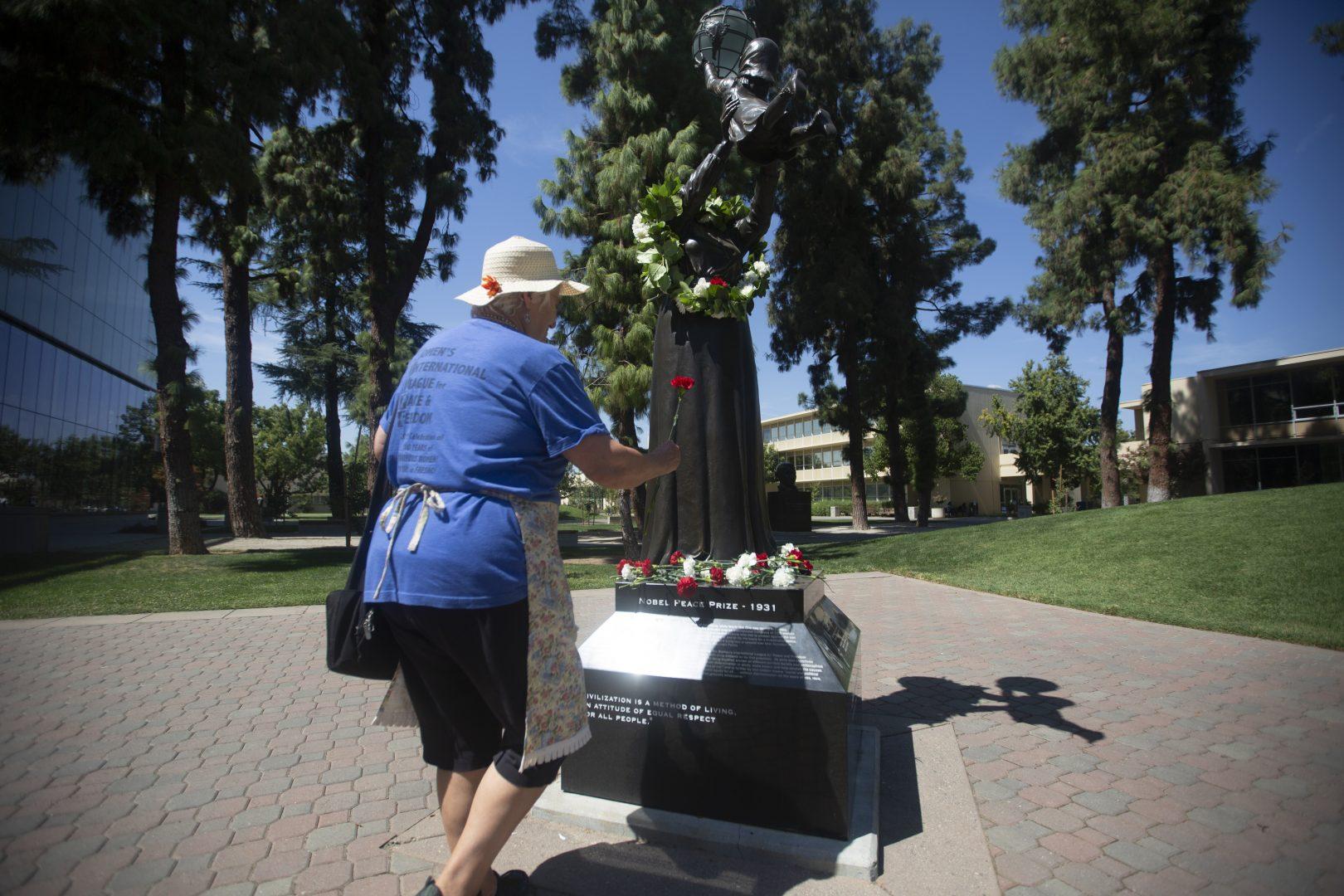 Member of The Raging Grannies Patty Bennett laying a rose at the feet of the Jane Addams statue at the Peace Garden during the annual commemoration of the statue on Friday, Sept. 13, 2019.  (Larry Valenzuela/ The Collegian)