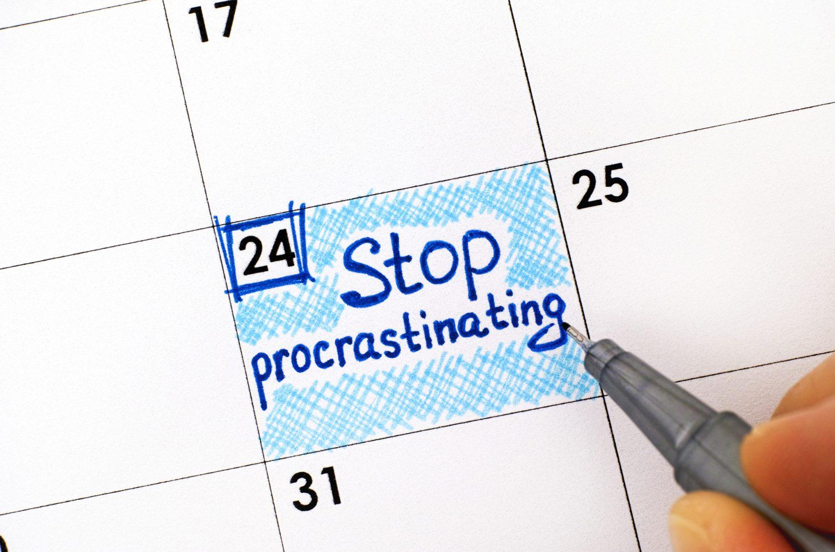 Woman fingers with pen writing reminder Stop Procrastinating in calendar. Close-up.