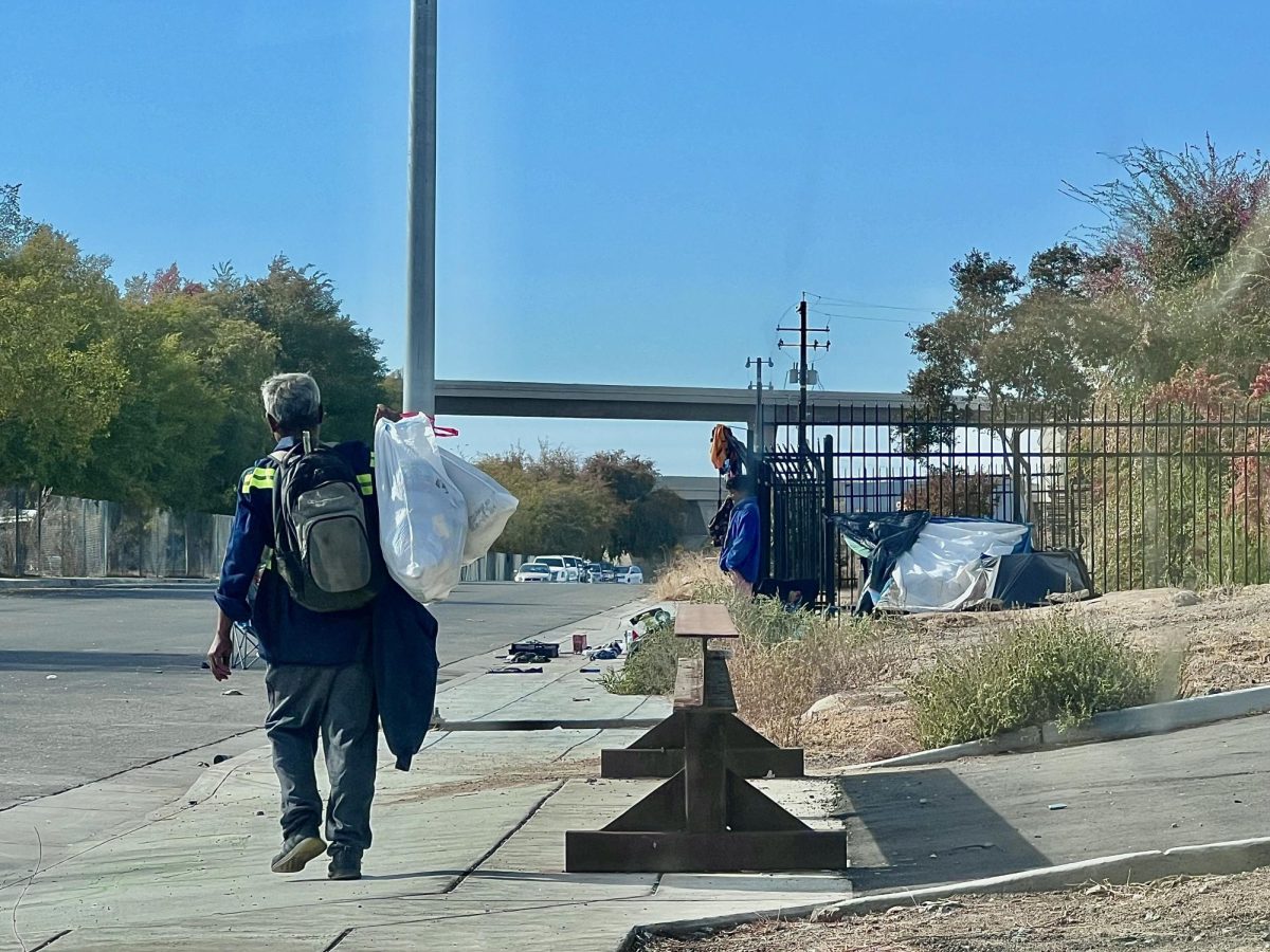 Unhoused man walks down a street in Fresno carrying his belongings over his shoulder. 