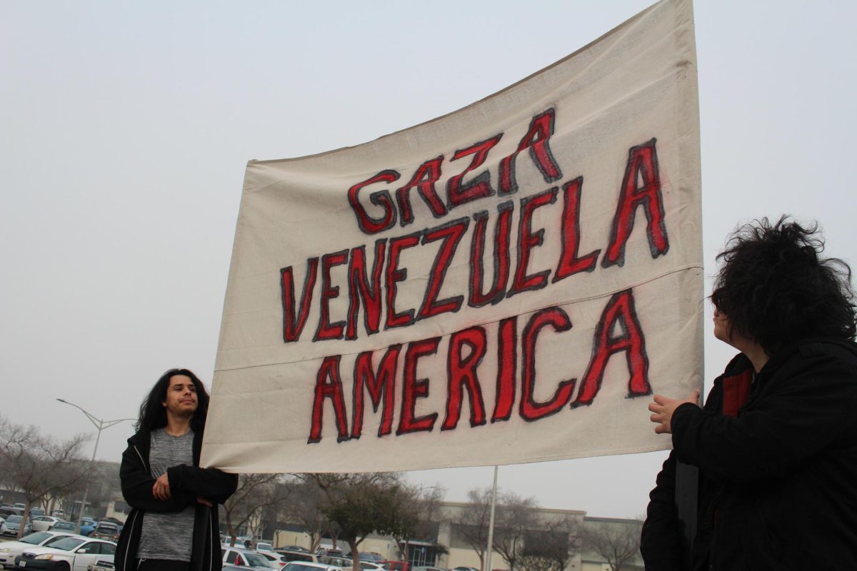 Two protesters stand holding a large sign facing cars passing by.