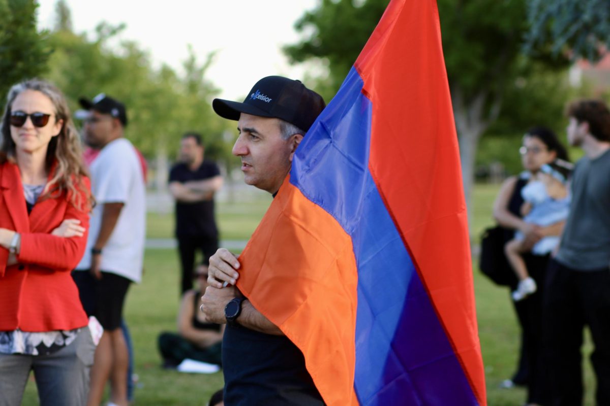 A man stands with an Armenian flag in hand, as he speaks to fellow ceremony attendees.